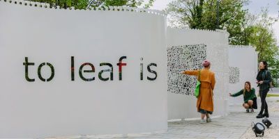 Three people look at a large grey rectangular sculpture with the words 