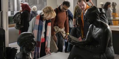 People stood in a museum looking at two bronze sculptures on a white plinth.