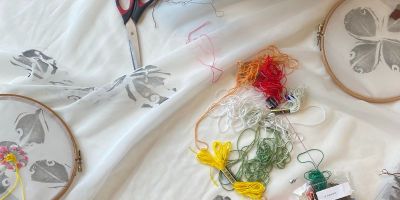 Two embroidery hoops in a patterned fabric, with various coloured threads and scissors laid out around them.