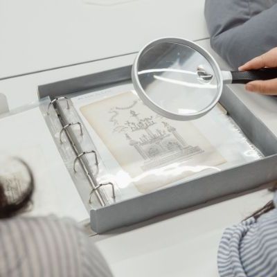 A top down view of two women looking at a document with a magnifying glass.
