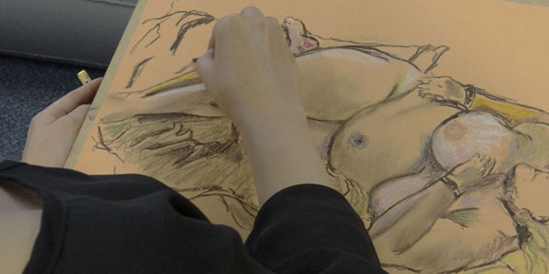 Hands doing a chalk drawing of a reclined figure