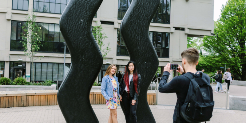 Students taking a photo in front of a two tall squiggly sculptures, an artwork called 'Sign for Art' by Keith Wilson