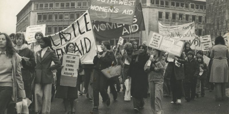 A black and white photo of women and children marching down the street with Women's Aid banners