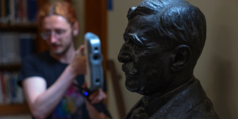 A photo of someone pointing imaging equipment at a dark bust sculpture.