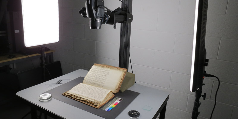 A manuscript book under a lighting set-up with two standing lights and digital recording equipment