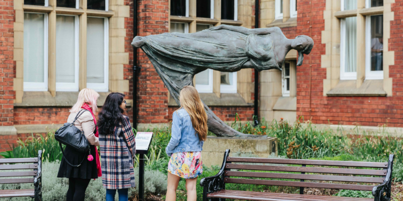 Three people standing admiring the sculpture ‘Levitating Figure, know as ‘The Dreamer’’ by Quentin Bell at the University of Leeds.