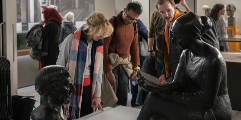 People stood in a museum looking at two bronze sculptures on a white plinth.