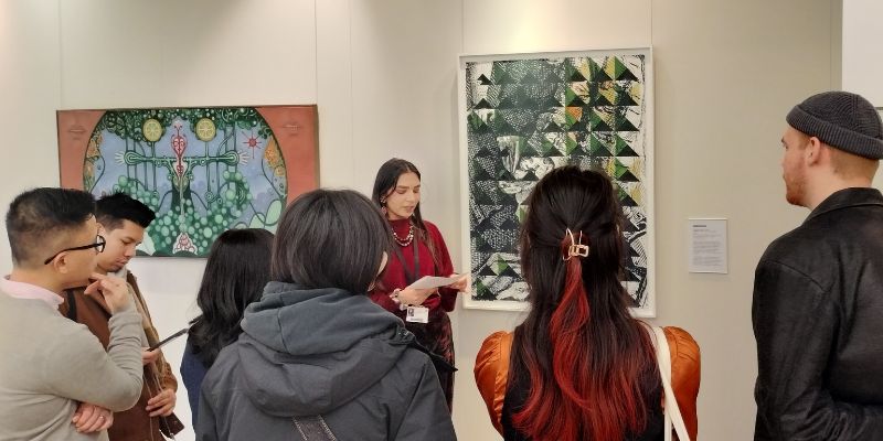 A person in a blue jumper holding a clipboard and drawing the artworks in a white gallery space