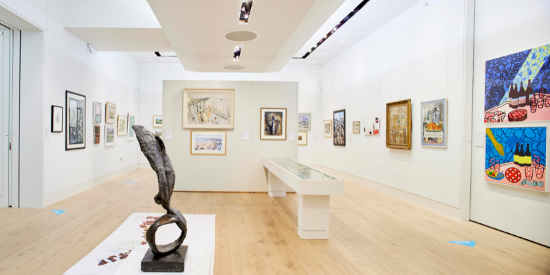 A brightly lit art gallery, showing a mixture of artworks, including sculpture, paintings and collage