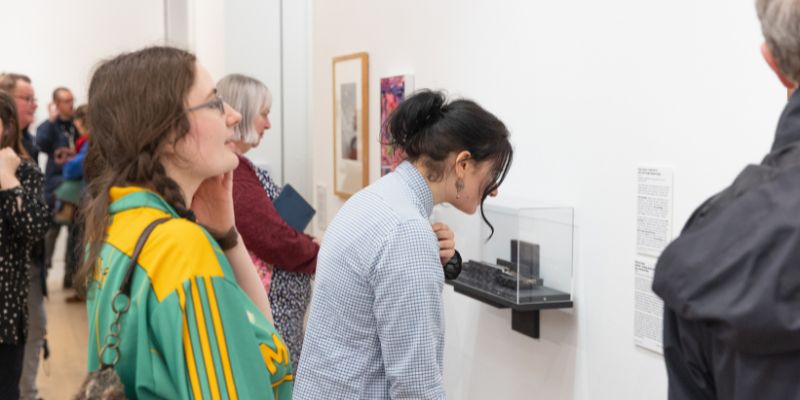 Visitors to an art gallery opening look at works hung on a white wall