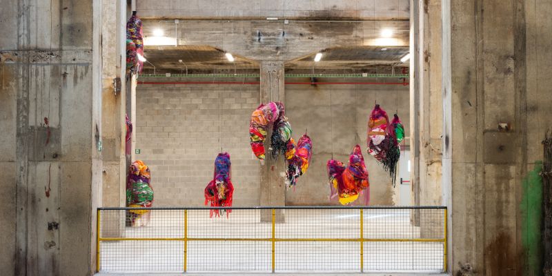 Various colourful textile sculptures hanging in an industrial concrete building.