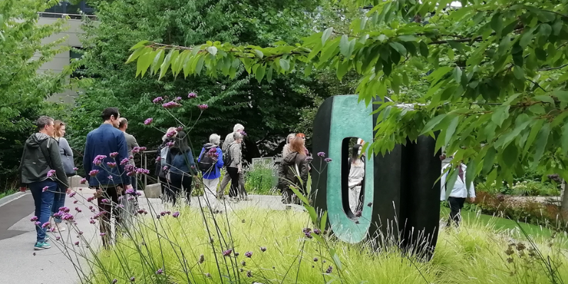 Group of people walking outside along a path beside a sculpture by Barbara Hepworth