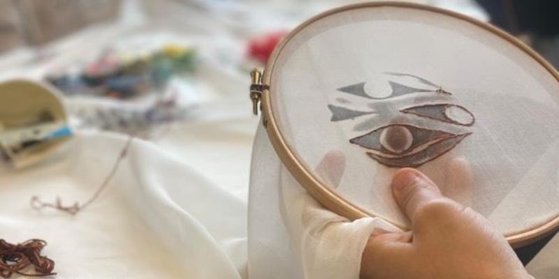 A hand holding an embroidery hoop with patterned fabric, in the middle of stitching a design.
