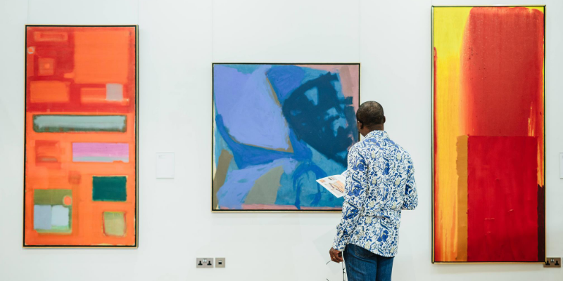 A man stands looking at 3 brightly coloured paintings in The Stanley and Audrey Burton Gallery