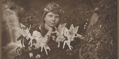 A sepia photograph of a little girl surrounded by dancing fairies