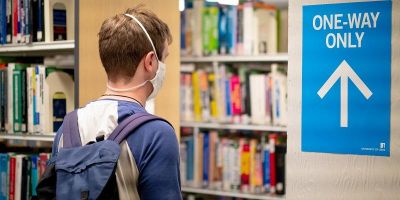 A mask-wearing student follows one-way signage in the library