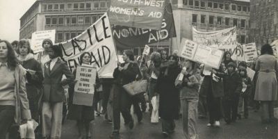 A black and white photo of women and children marching down the street with Women's Aid banners