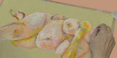 A hand drawing a nude figure in yellow and pink pastels on yellow paper.