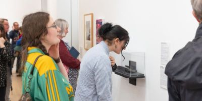 Visitors to an art gallery opening look at works hung on a white wall