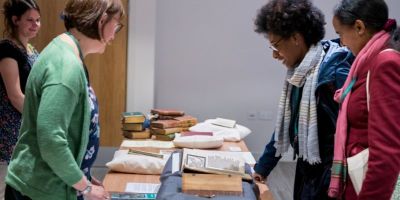 People stood either side of a table filled with open books resting on cushions.