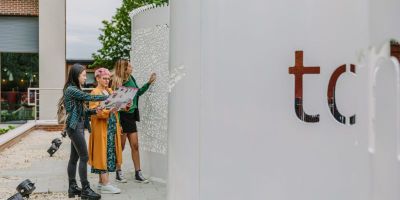 Three people looking at a map stood by a white metal sculpture with patterns and letters cut from it.