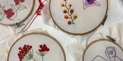 Four embroidery hoops attached to a white fabric. Inside each is an embroidery of flowers, plants or fruit.