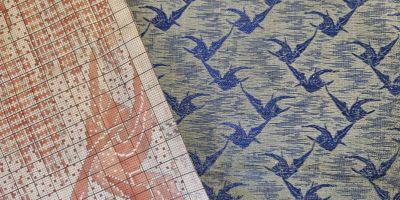 A textile pattern in pink on white graph paper, over a blue and white patterned fabric of birds