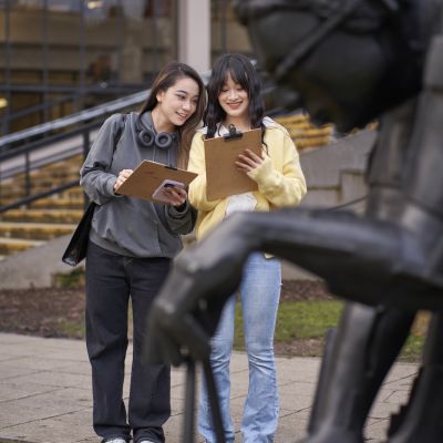 Two people stand looking at a map of the public art trail. In front of them, partially in shot, is a Eduardo Paolozzi's statue