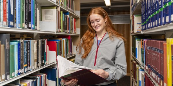 A student is reading a book in Library while smiling.