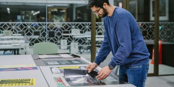 A man stands at a table leafing through a stack of posters.