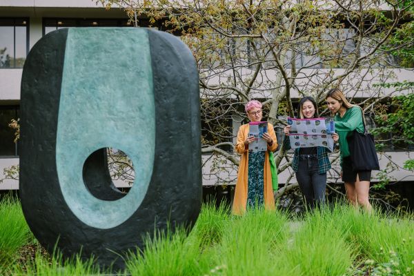 Three people stand looking at paper maps of the public art trail. A large abstract sculpture is in front of them.