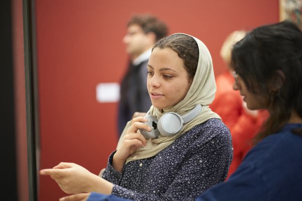 A visitor in a head covering and over ear headphones points to an artwork in The Stanley & Audrey Burton Gallery.