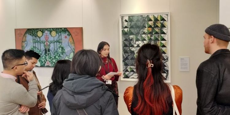 A group of students stood in The Stanley &amp; Audrey Burton Gallery listening to a talk being given by a member of staff about one of the artworks on display.