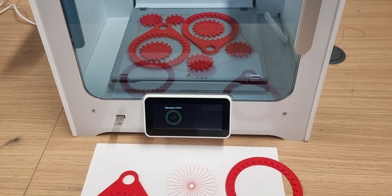 Red fabricated cogs sit in a 3D printer