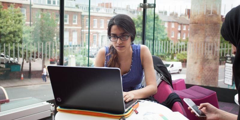 A student sitting next to a window working on a laptop computer