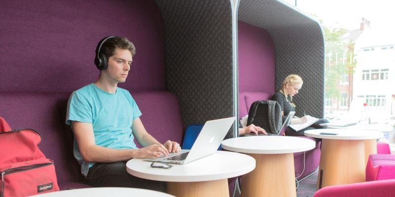 Two students sat near a window on high backed furniture