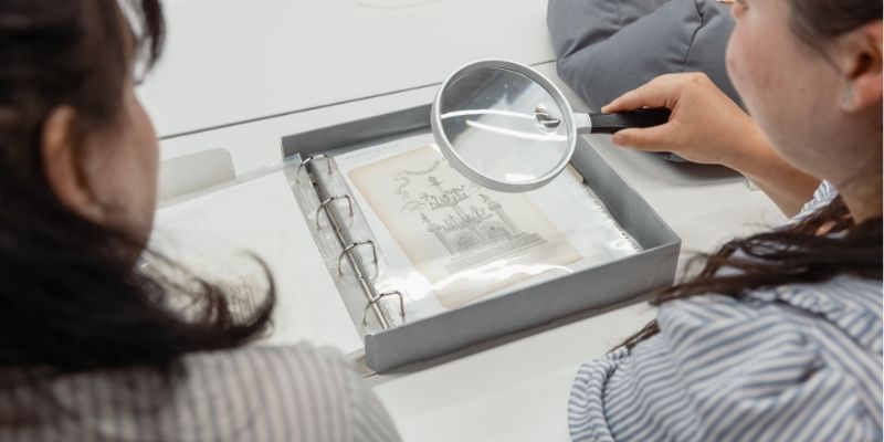 A top down view of two women looking at a document with a magnifying glass.