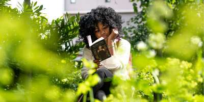 A student reads The Great Gatsby among the greenery on campus